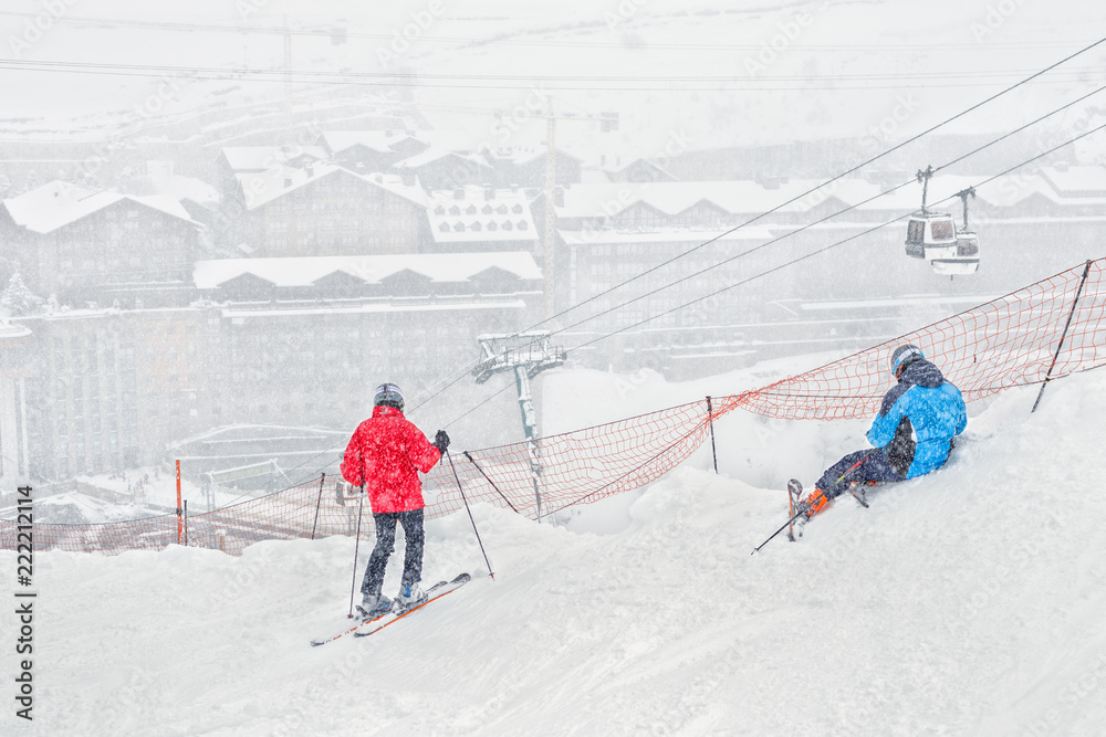 Two skiers have a rest on a slope during a heavy snowfall