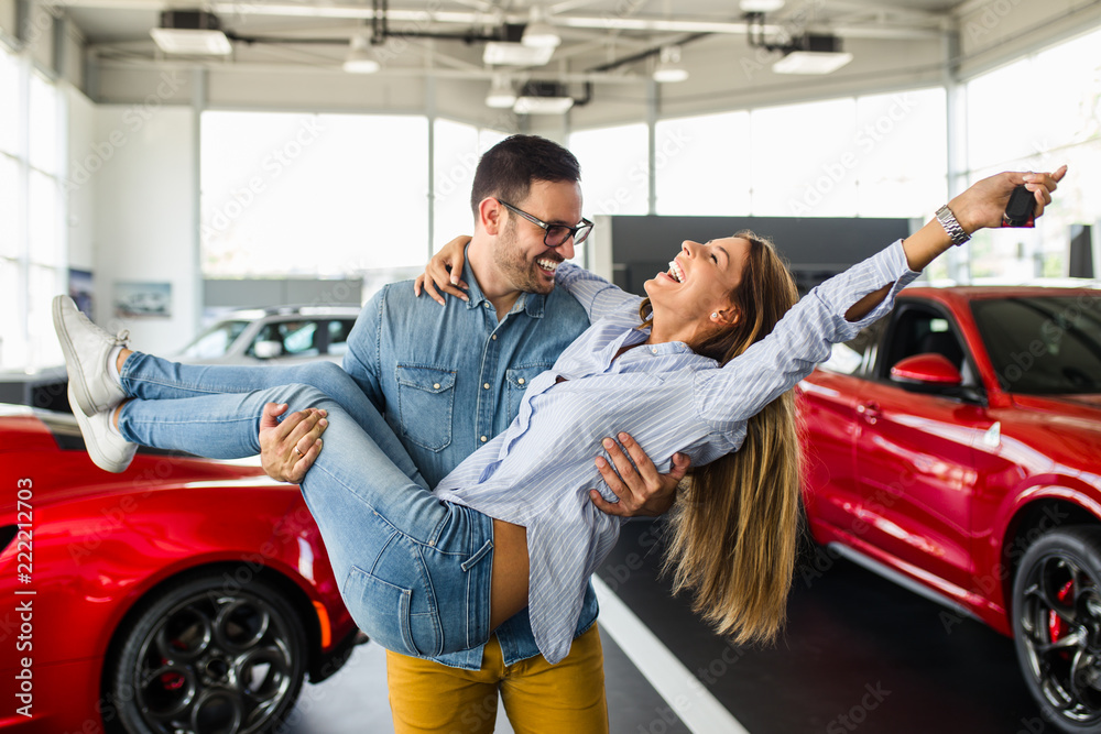 Beautiful young couple at car showroom exited because of buying a new car. Beautiful young couple at car showroom exited because of buying a new car.