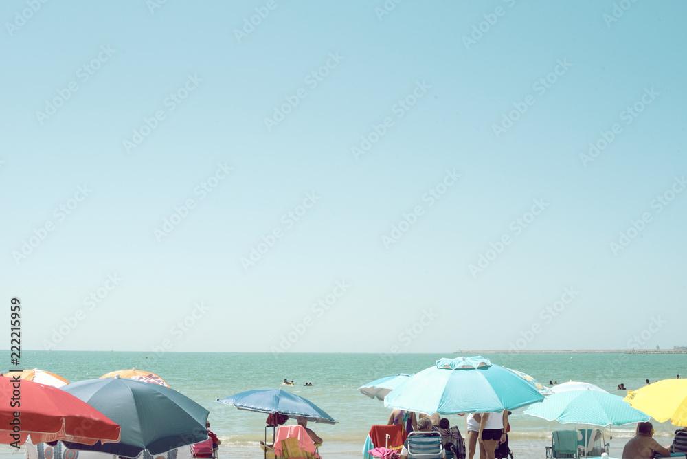 Imagen veraniega de sombrillas coloridas en una playa llena de gente frente a un mar en calma un día de verano despejado