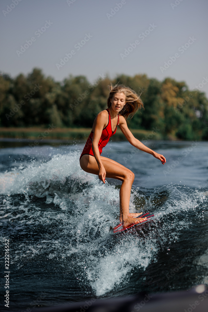 Blonde girl riding on the red wakeboard on the lake