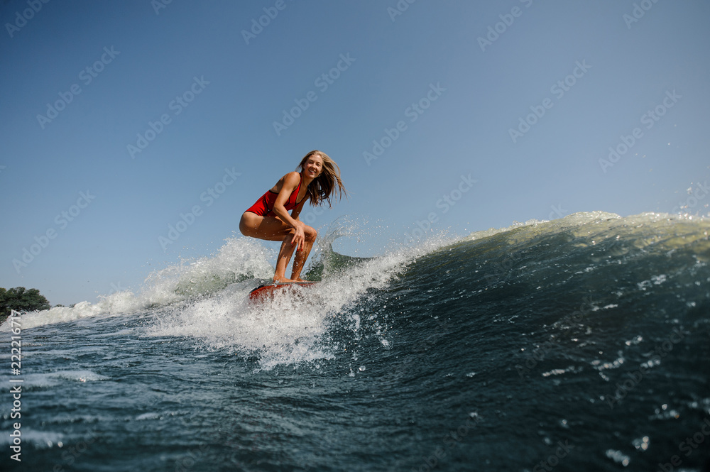 Smiling blonde girl standing on the wakeboard on the lake