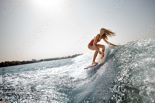 Active blonde girl standing on the wakeboard on the lake