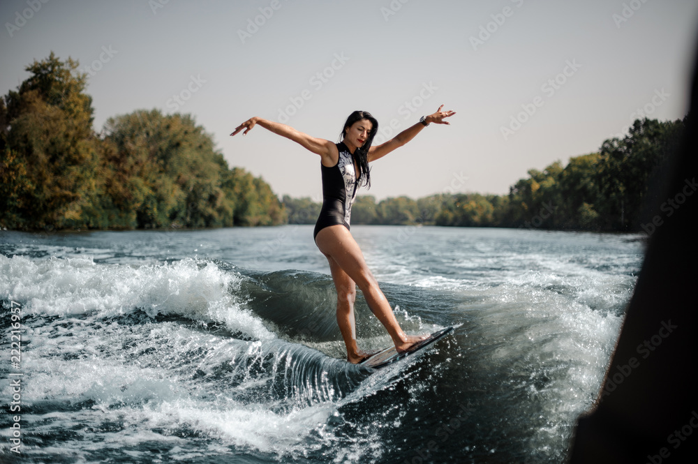 Fototapeta premium Brunette girl riding on the wakeboard keep her hands up