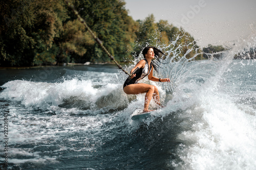Fotografie, Obraz Smiling brunette girl riding on the wakeboard holding a rope