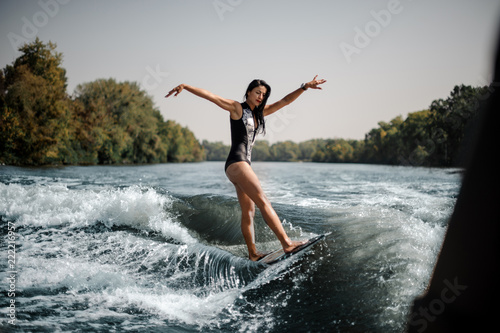Brunette girl riding on the wakeboard keep her hands up