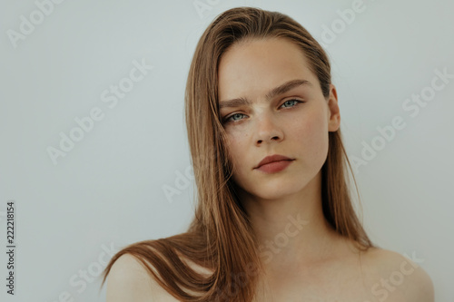 Portrait of attractive young girl with long hair and bare shoulders is looking at camera, isolated on white, copy spase