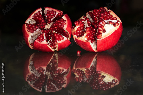 Two opened pomegranates resting on glass reflecting surface