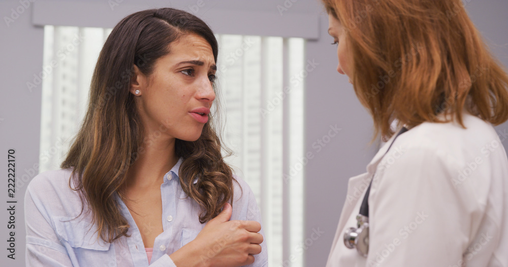Close up of charming hispanic patient meeting with doctor about shoulder injury. Portrait of attractive latina discussing her arm trauma with mid aged medical doctor indoors office Close up of charming hispanic patient meeting with doctor about shoulder injury. Portrait of attractive latina discussing her arm trauma with mid aged medical doctor indoors office