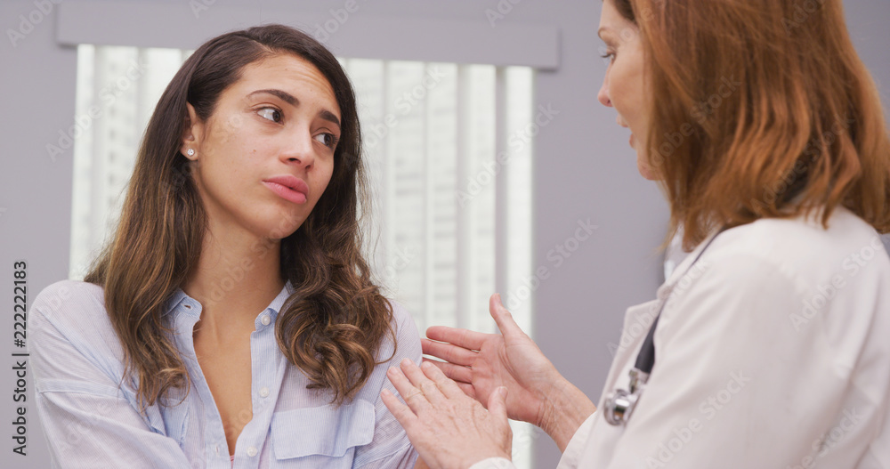 Close up of charming hispanic patient meeting with doctor about shoulder injury. Portrait of attractive latina discussing her arm trauma with mid aged medical doctor indoors office Close up of charming hispanic patient meeting with doctor about shoulder injury. Portrait of attractive latina discussing her arm trauma with mid aged medical doctor indoors office
