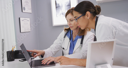 Portrait of two medical physicians looking at lab results of patient on laptop computer. Close up of senior medical doctor discussing ct scans on computer with young colleague