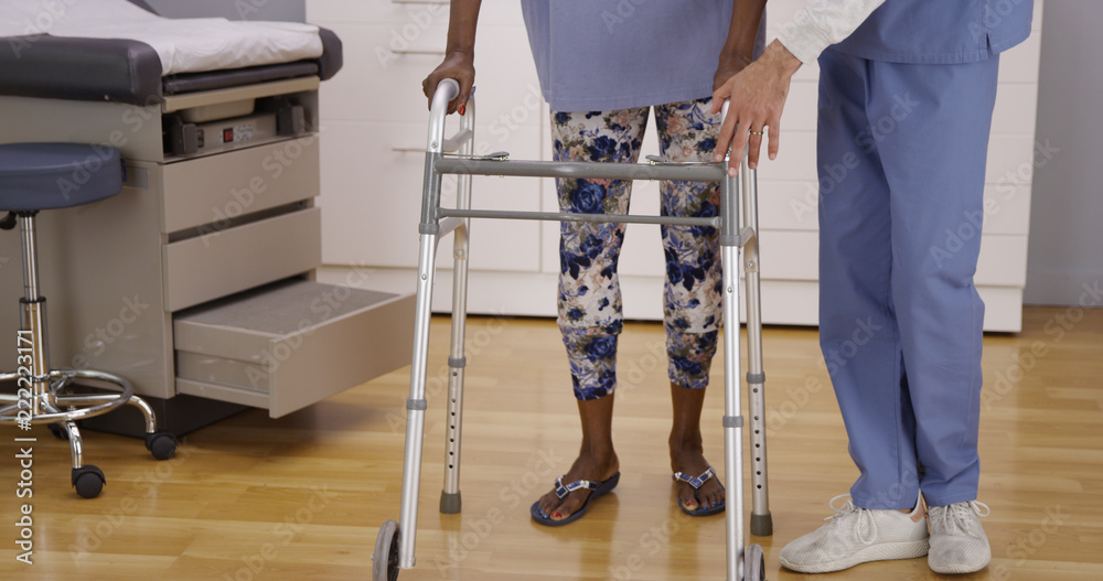 Young male nurse helps senior black woman walk with crutches. Middle