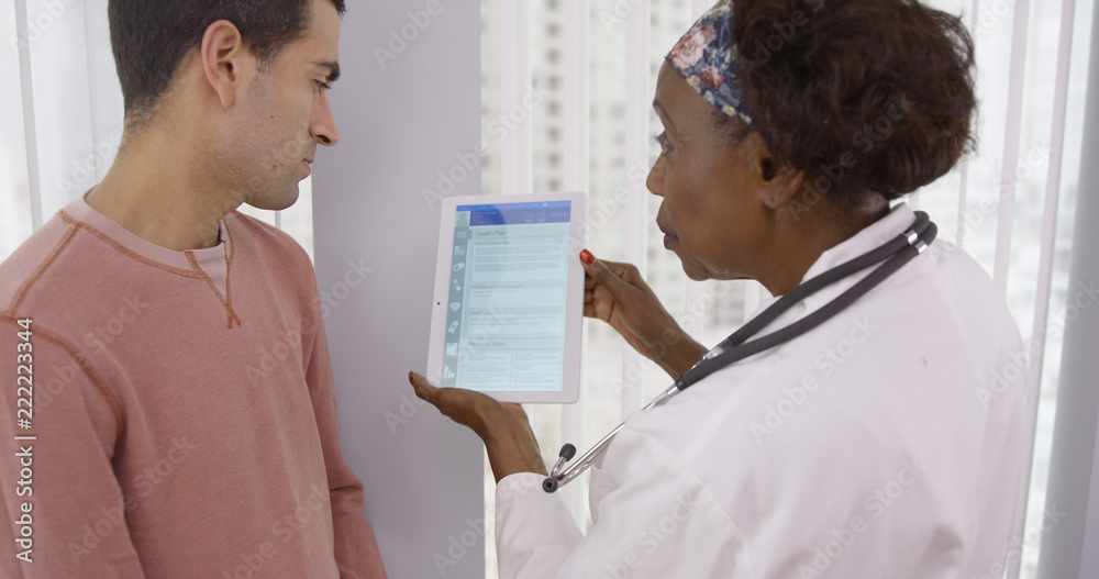 Ταπετσαρία Mid aged black doctor using electronic notebook tablet to share different health plans with young male patient
