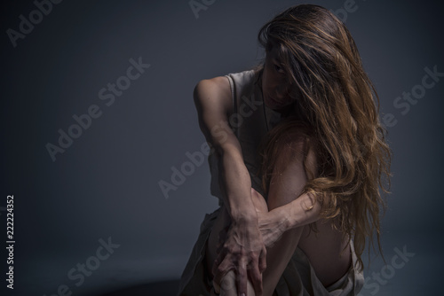 Depressed young woman sitting in a dark corner, crushed and alone