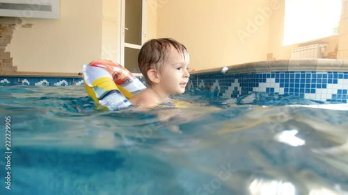 4k video of little boy with inflatable ring swimming in undoor swimming pool photo