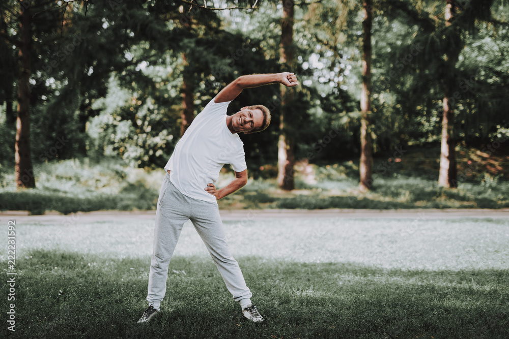 Man in White Sportswear Doing Exercises in Park. Man in White Sportswear Doing Exercises in Park.