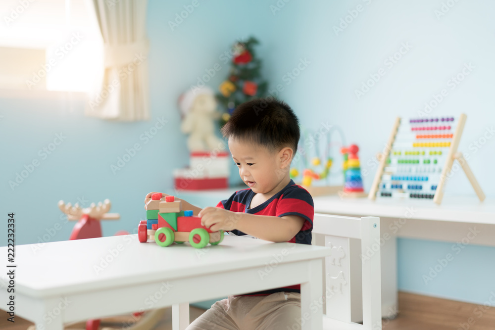 Adorable Asian Toddler baby boy sitting on chair and playing with color wooden train toys at home.. Adorable Asian Toddler baby boy sitting on chair and playing with color wooden train toys at home..
