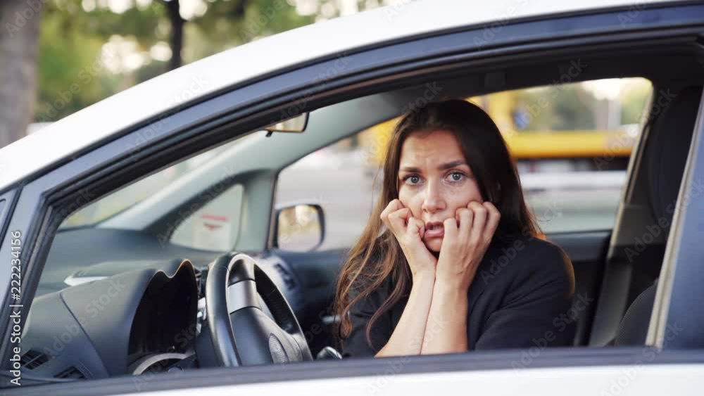 The frightened woman is sitting behind the car and looking in the window. 4K UHD video. The frightened woman is sitting behind the car and looking in the window. 4K UHD video.