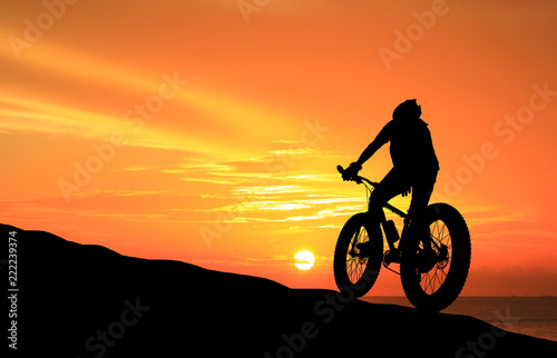 Silhouette man and bike relaxing on blurry sky background.