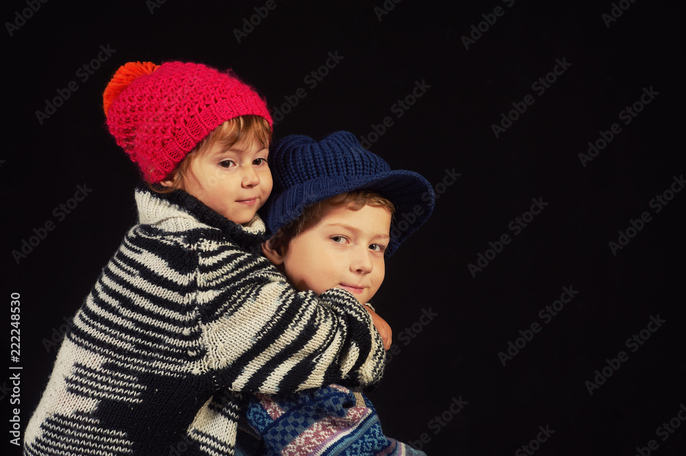 children in warm knitted hats on a dark background . Brother and sister in warm sweaters children in warm knitted hats on a dark background . Brother and sister in warm sweaters
