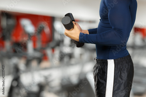 Torso shot of a young man lifting dumbbells. Fit young man exercising with dumbbells on gym background