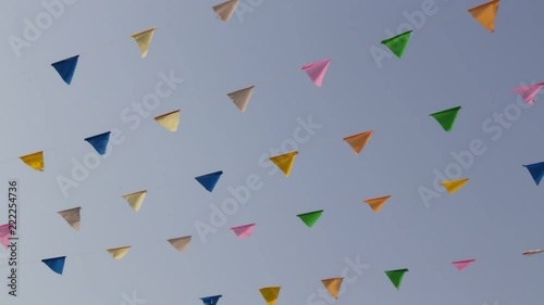 HD video footage of rows of colorful triangle flags hung from lines of cables blowing in the wind on blue sky background in a celebration festival