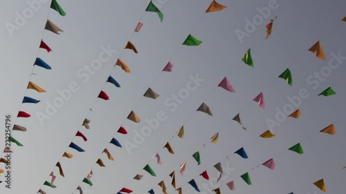 HD video footage of rows of colorful triangle flags hung from lines of cables blowing in the wind on blue sky background in a celebration festival