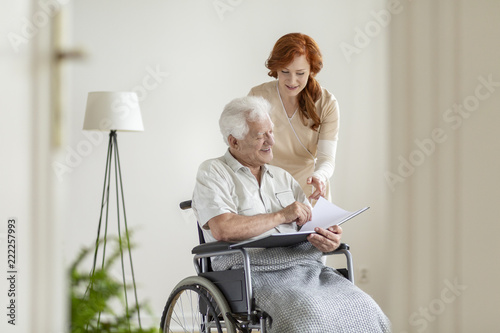 Nurse and patient in a wheelchair looking at photo album together and smiling photo