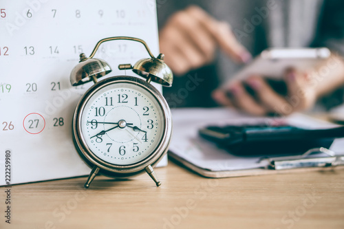 due date calendar and alarm clock with blur business woman hand calculating  monthly expenses during tax season. photo