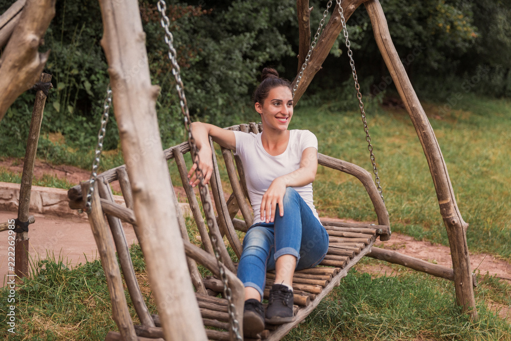 The happy young woman sitting on the swing outdoors