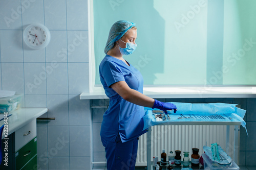 Fotografija Young blond woman assistant standing near table with equipment prepating for gynecology operation