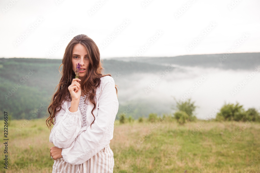 Portrait of the pretty young woman standing on nature  and holding flowers