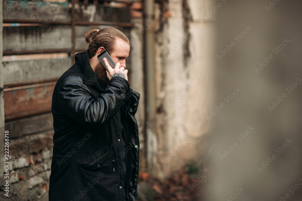 A bearded man in a black leather jacket stands outside and poses for a photographer. Use a phone A bearded man in a black leather jacket stands outside and poses for a photographer. Use a phone