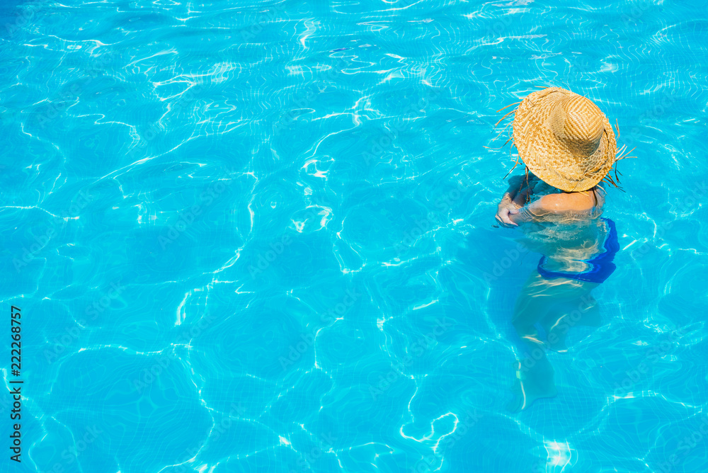 Woman in a pool with hat relaxed and rested.