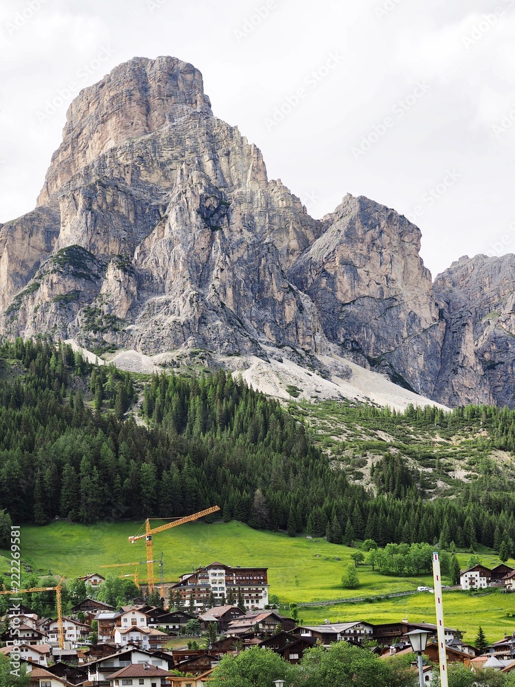 A picturesque panorama in the Dolomites. There are huge mountains covered with snow, coniferous forests, mountain clear azure lake, a lonely wild place, a deserted hut in the forest