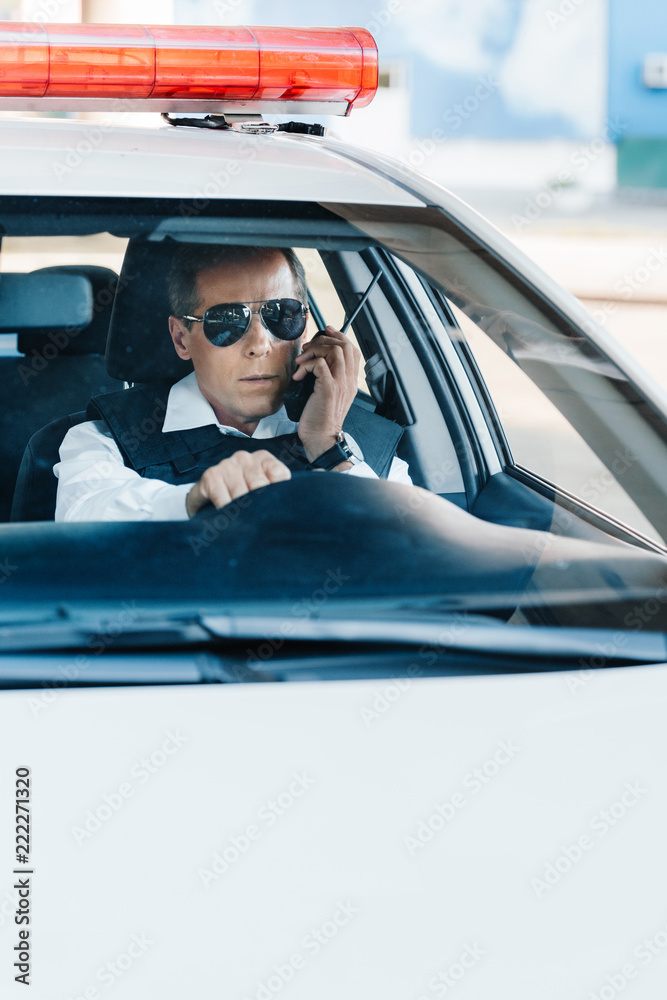 middle aged policeman in sunglasses talking on radio set in car