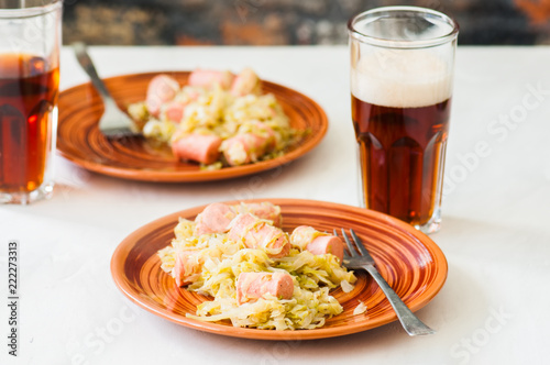 Traditional dish of german cuisine - Cabbage stew with grilled sausage with glass of beer. White stone background.