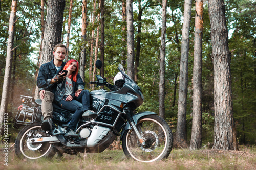 Outdoor shot of happy young romantic couple with big motorcycle for tourism and travel. autumn forest background, traveling together, off road, red hair girl