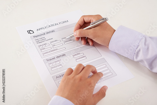 Hands of anonymous person writing down personal information in application form on white background