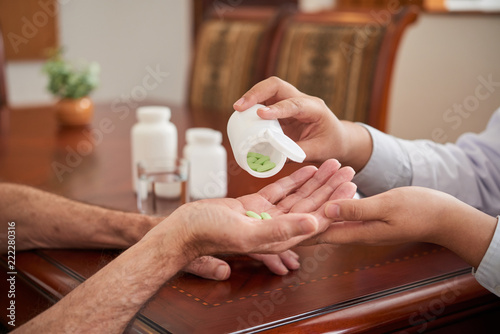 Crop shot of doctor putting pills in hand of senior man sitting at table