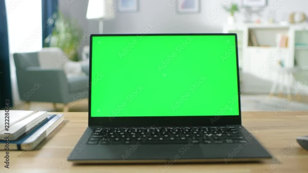 Zoom in on a Modern Laptop with Green Mock-up Screen Display Standing on the Desk of the Cozy Living Room. 
