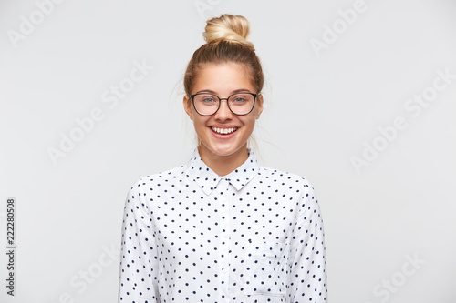 Closeup of smiling pretty young woman with bun wears polka dot shirt and glasses feels happy and confident isolated over white background