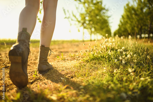 View on legs and shoes of walking girl in the green orchard by the path, during sunny day.