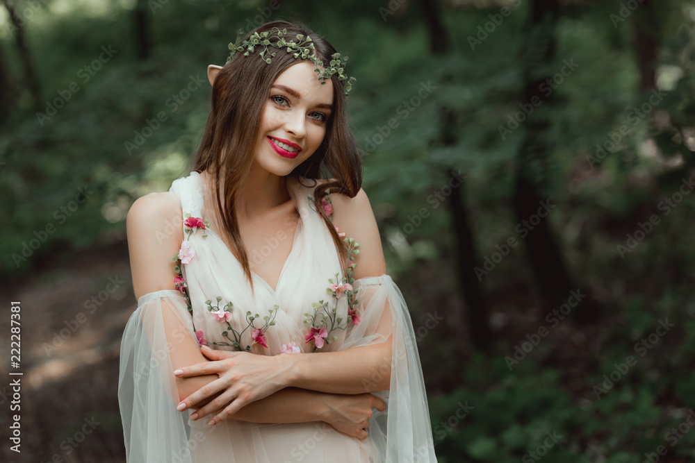attractive smiling girl in dress and floral wreath posing in woods attractive smiling girl in dress and floral wreath posing in woods