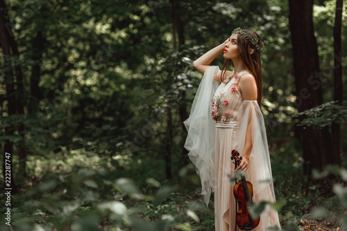 mystic elf character in flower dress holding violin in green forest