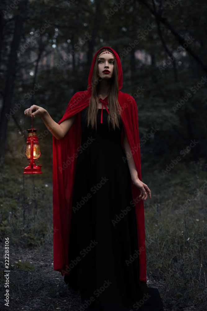 young mystic woman in red cloak with kerosene lamp walking in dark woods young mystic woman in red cloak with kerosene lamp walking in dark woods