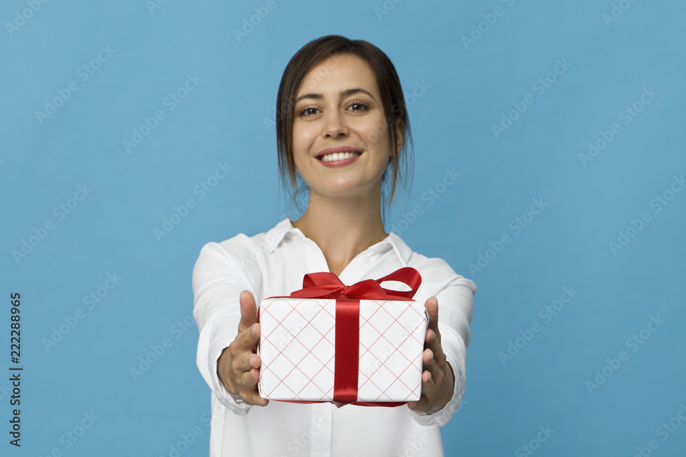 Beautiful woman holding a gift box with red ribbon. Isolated on blue background Beautiful woman holding a gift box with red ribbon. Isolated on blue background