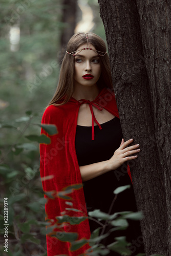 beautiful mystic girl in red cloak and elegant wreath in forest