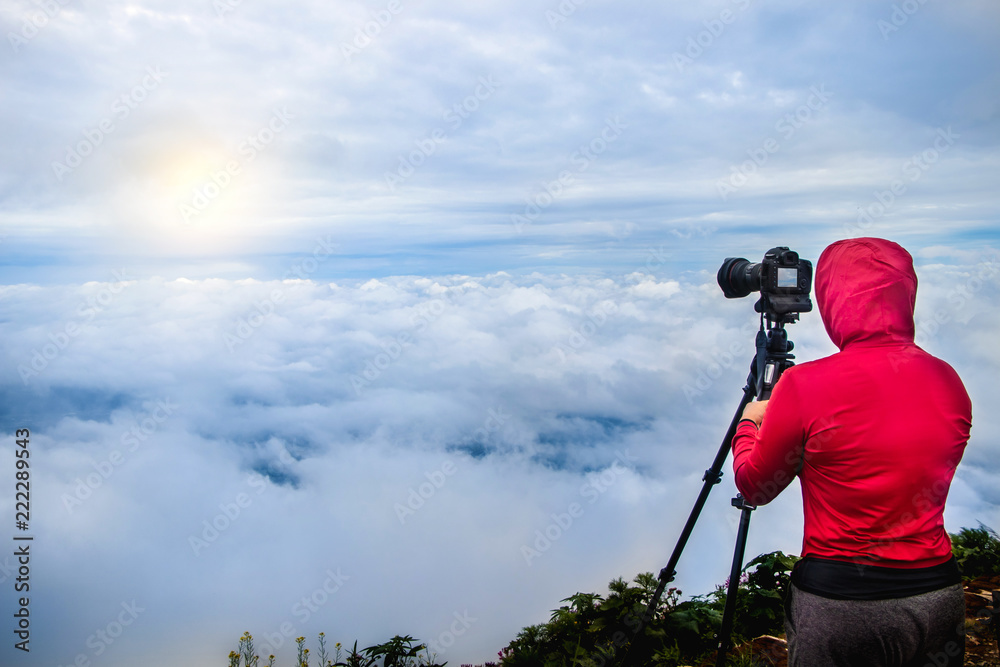 Photographer taking Thailand travel nature photography. Woman photographer shooting with tripod and DSLR camera in sunset with beautiful landscape in background.