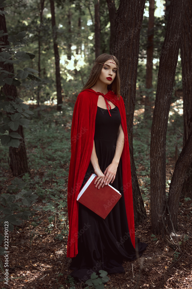 cropped view of mystic girl in red cloak holding magic book in forest cropped view of mystic girl in red cloak holding magic book in forest