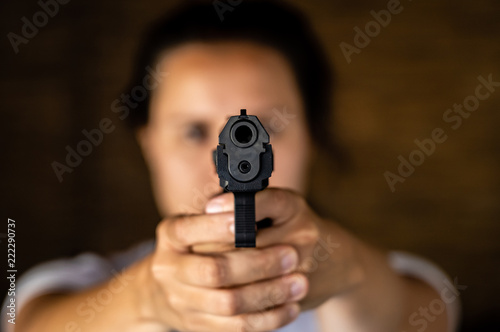 Young woman holding a gun and aiming toward a camera. Pistol in hand and pointing.
